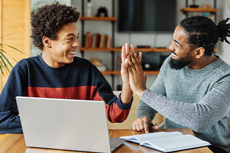 Student and teacher high five with laptop and book